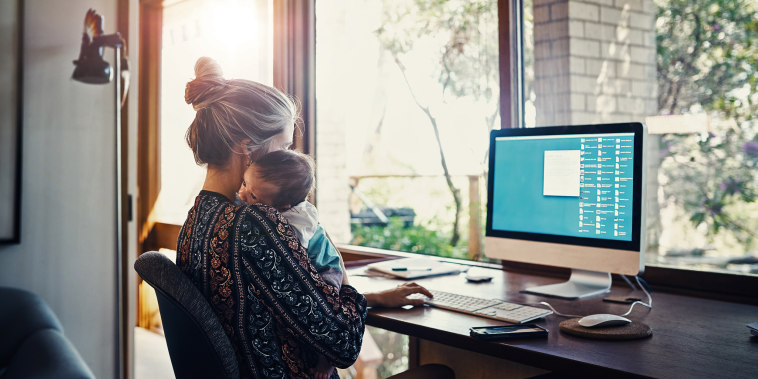 young woman working at home while holding her newborn baby son