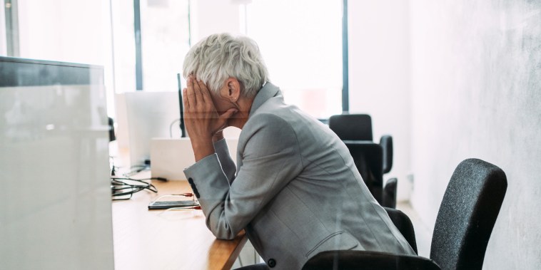 A woman holds her head in her hands at a desk.